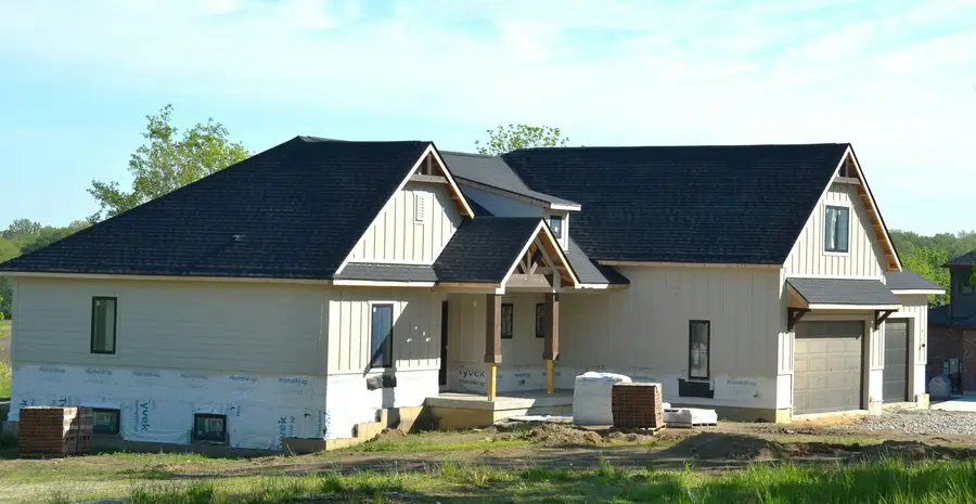 New farmhouse-style house with white board-and-batten siding and a dark roof on an open lot