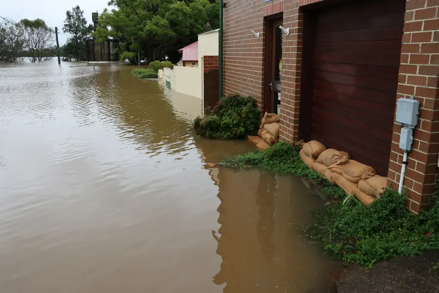 Sandbags stacked against a brick house wall in brown floodwater